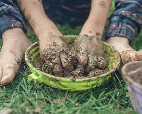 A child's dirty hands are shown in a bowl that's sitting atop grass.